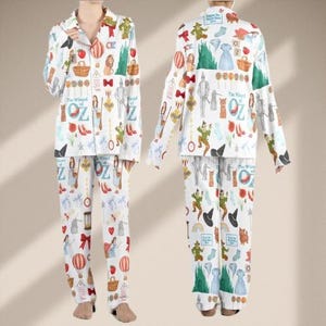 May include: White pajama set featuring a colorful print of characters and icons from The Wizard of Oz. The long-sleeved top and pants are covered in illustrations of Dorothy, the Tin Man, the Wicked Witch, and more. The words "The Wizard of Oz" are also printed on the pajamas.