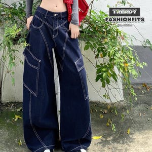 Könnte beinhalten: Dunkelblaue Denim-Cargohose mit weißen Nähten. Die Hose hat große Taschen und ein weites Bein. Der Text "TRENDY FASHIONFITS" ist sichtbar. Unisex-Mode.