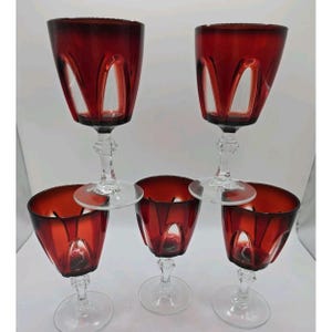 Puede incluir: Un juego de cinco copas de vino con cuencos de color rojo intenso y patrones de arco recortados en vidrio transparente. Cada copa tiene un tallo transparente facetado y una base circular. El diseño combina un tono carmesí vibrante con secciones transparentes.