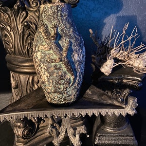 May include: A green ceramic vase with a textured surface and a raised design of a figure. The vase is sitting on a black, ornate table.
