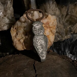 May include: A silver owl-shaped bottle opener with a rusty brown metal ring.