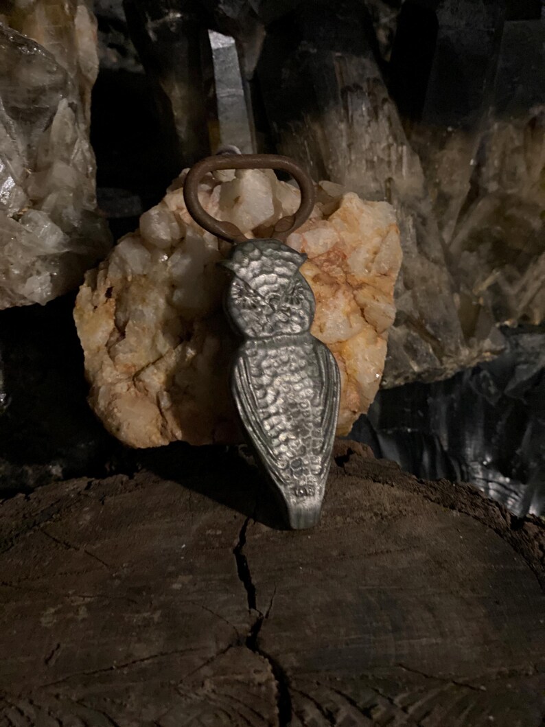 May include: A silver owl-shaped bottle opener with a rusty brown metal ring.