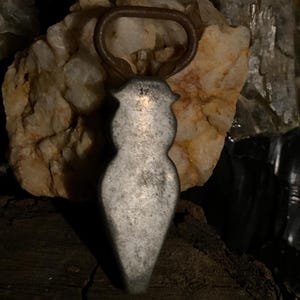 May include: A silver bottle opener shaped like a woman's body. The opener has a rusty ring at the top.