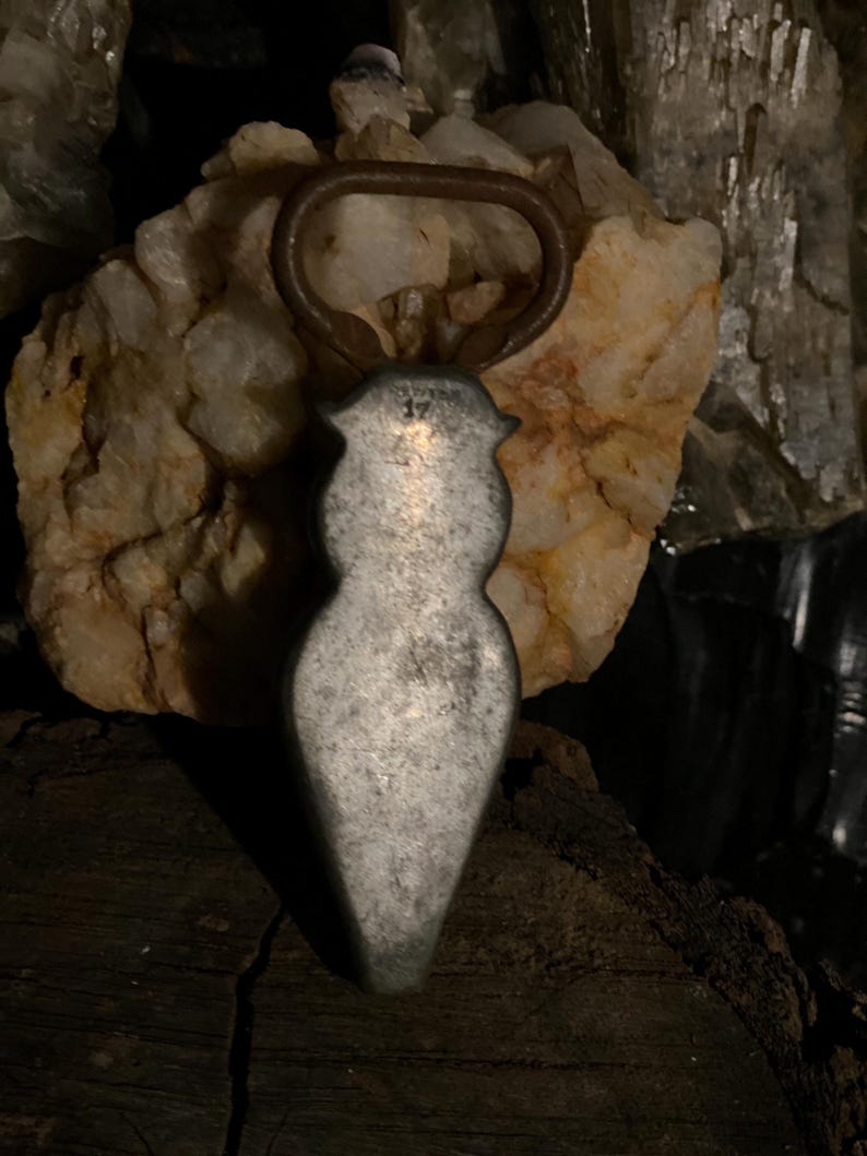 May include: A silver bottle opener shaped like a woman's body. The opener has a rusty ring at the top.