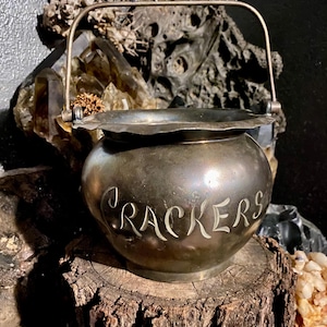 May include: A silver-toned metal cracker jar with a decorative handle and the word "Crackers" engraved on the side.