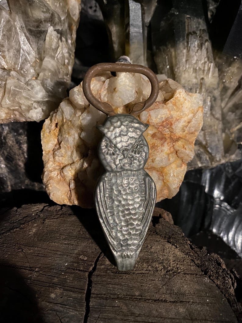 May include: A silver owl bottle opener with a rusty metal ring. The opener is sitting on a piece of wood.