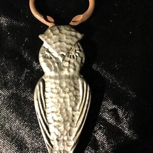 May include: A silver owl bottle opener with a textured surface and a brown metal loop.