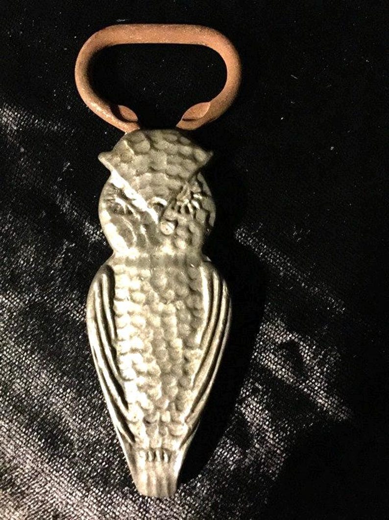 May include: A silver owl bottle opener with a textured surface and a brown metal loop.