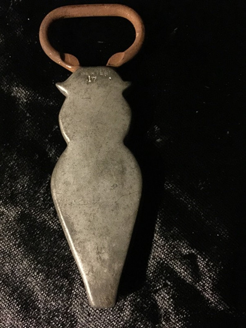 May include: A silver bottle opener with a copper handle. The opener is shaped like a person and has the word "PEWTER" and the number "17" engraved on it.