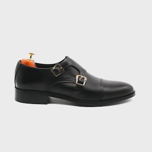 Puede incluir: Zapato de doble hebilla de cuero negro con puntera. El zapato presenta dos hebillas doradas y un tac&oacute;n bajo. Dise&ntilde;ado para vestimenta formal o de negocios.