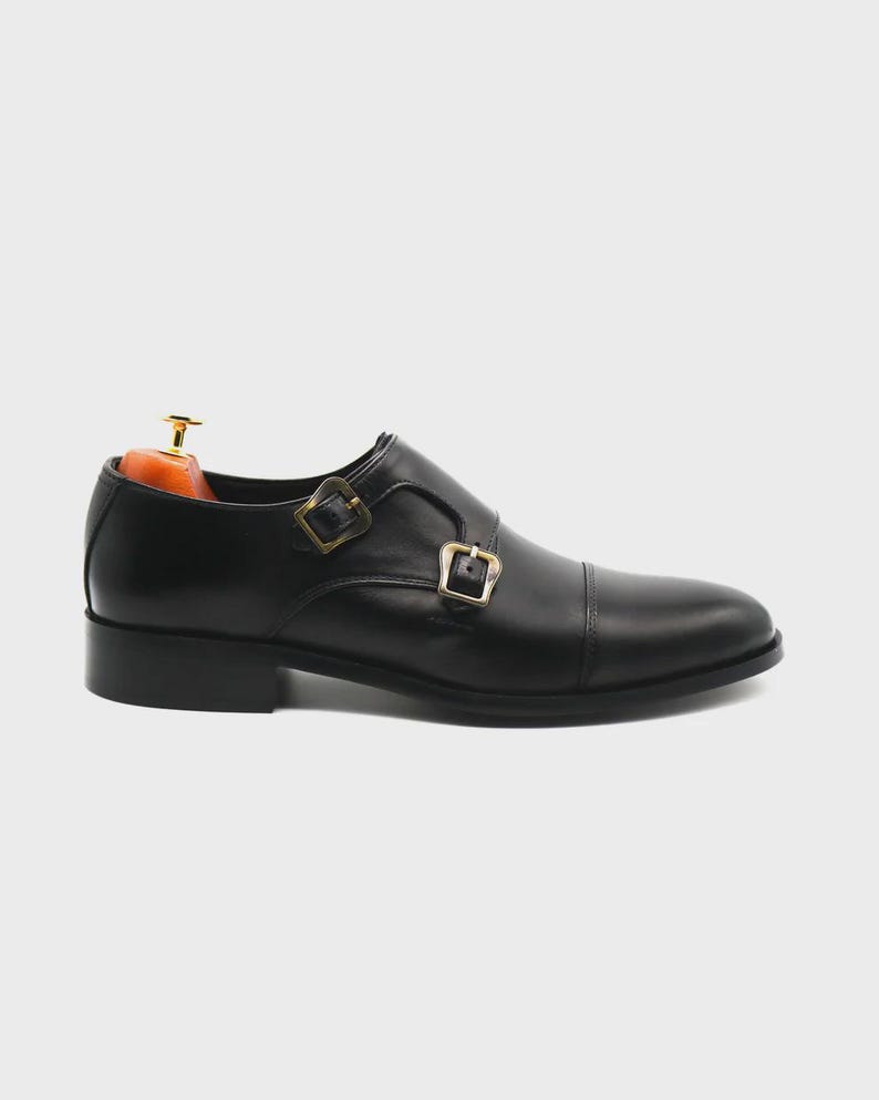 Puede incluir: Zapato de doble hebilla de cuero negro con puntera. El zapato presenta dos hebillas doradas y un tac&oacute;n bajo. Dise&ntilde;ado para vestimenta formal o de negocios.
