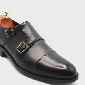 Puede incluir: Zapato negro de cuero con doble hebilla y hebillas doradas. El zapato presenta un dise&ntilde;o de puntera y un horma de madera en el interior. El zapato est&aacute; dise&ntilde;ado para uso formal.