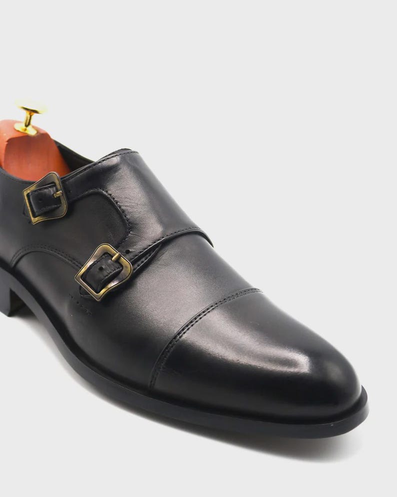 Puede incluir: Zapato negro de cuero con doble hebilla y hebillas doradas. El zapato presenta un dise&ntilde;o de puntera y un horma de madera en el interior. El zapato est&aacute; dise&ntilde;ado para uso formal.