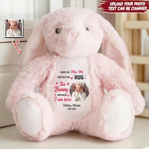 May include: A soft, pink plush bunny with long ears. The bunny features a personalized design on its chest, including a photo, text that reads "When you miss me, have no fear, hug," and the name "Whitley Martin 1945-2025."