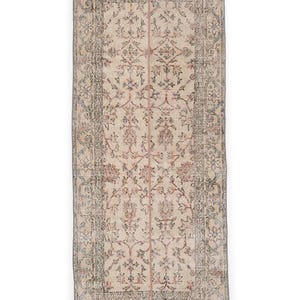 May include: A rectangular, vintage-style rug with an intricate floral pattern. The rug features a cream-colored background with faded accents of blue, red, and gray. The edges are bordered with a detailed design, and a vertical stripe runs down the center.