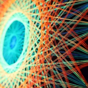 Può includere: Opera d'arte astratta con un design geometrico. L'immagine mostra una forma centrale a forma di occhio in tonalità turchese e blu, circondata da linee radianti arancioni e verdi su sfondo nero. L'opera ha un'estetica moderna e artistica.