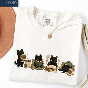 Camiseta fofa de gato preto para amantes de livros, camiseta aconchegante com gatos lendo, camiseta de gatinho leitor, presente para bibliófilos, camiseta com cores confortáveis e estética de leitor.