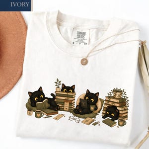 Camiseta fofa com gato preto lendo, camiseta aconchegante para amantes de livros, camiseta com gatinho leitor, presente para bibliófilos, camiseta com cores confortáveis e estética de leitor.