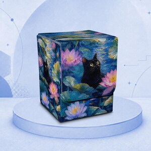 May include: A square deck box featuring a vibrant, painterly print of a black cat nestled among colorful pink and purple water lilies and green lily pads. The box has a structured, upright design with a hinged lid, showcasing a detailed artistic scene.