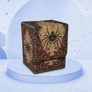 Puede incluir: Una caja para barajas cuadrada con fondo color canela y una ilustración de una araña negra centrada en la tapa. Los lados y la tapa están decorados con un patrón floral oscuro de rosas rojas y filigrana negra sobre una telaraña.