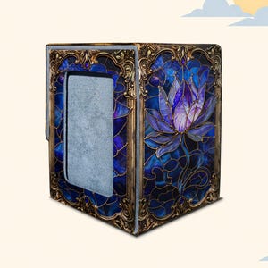 May include: A rectangular box with a hinged lid featuring a stained glass style design of a purple lotus flower on a deep blue background. The box is framed with ornate, antique gold-colored metal trim and has a grey, textured interior lining.