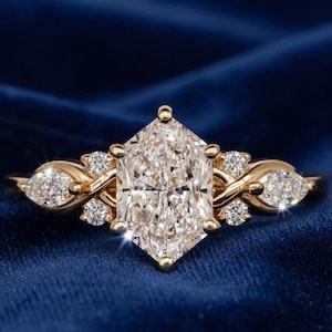 Könnte beinhalten: Ein Goldring mit einem großen, zentralen Edelstein im Hexagonschliff, der auf beiden Seiten von zwei kleineren Steinen im Marquiseschliff flankiert wird. Die Ringschiene ist gedreht und mit vier winzigen runden Steinen verziert.