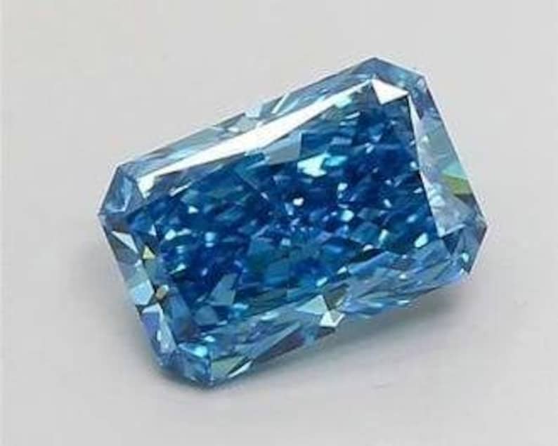K&ouml;nnte beinhalten: Ein Fancy Vivid Blue Diamant im Radiant-Schliff. Der Edelstein hat eine rechteckige Form mit vielen Facetten, die das Licht reflektieren. Die Farbe des Diamanten ist ein tiefes, sattes Blau, vor wei&szlig;em Hintergrund.
