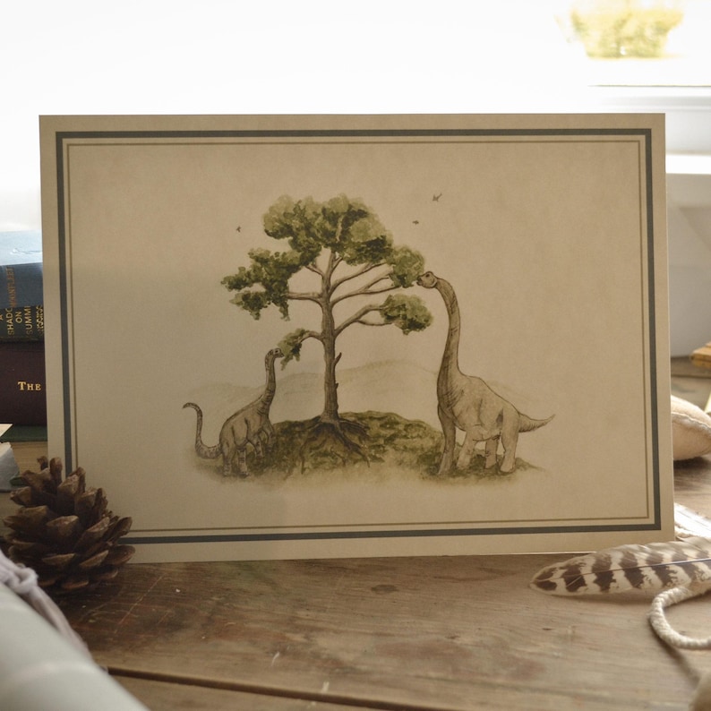 May include: A framed print featuring two dinosaurs reaching up to eat leaves from a tree. The artwork is in muted tones of green, brown, and beige, with a simple border. The dinosaurs have long necks and are standing on a grassy area.