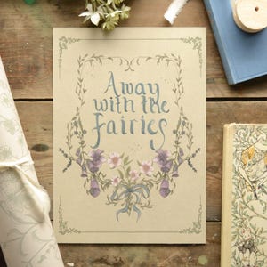 May include: A beige card with the text "Away with the Fairies" in blue script, framed by a floral and leaf design. The card features purple flowers and a blue ribbon. Other items include a book and wrapping paper.