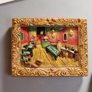 May include: A rectangular, gold-framed relief sculpture depicting Van Gogh's "The Night Cafe." The artwork features a yellow-lit interior with a pool table, figures, and a red and yellow color scheme. The frame has ornate, swirling details.