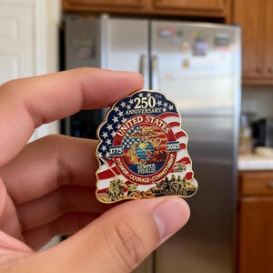 K&ouml;nnte beinhalten: Eine goldfarbene Anstecknadel zum 250. Jahrestag der Vereinigten Staaten. Die Anstecknadel zeigt die amerikanische Flagge, die Worte "United States", "250th Anniversary" und die Jahre 1775 und 2025. Sie enth&auml;lt auch die Worte "Honor, Courage, Commitment" und "Semper Fidelis."