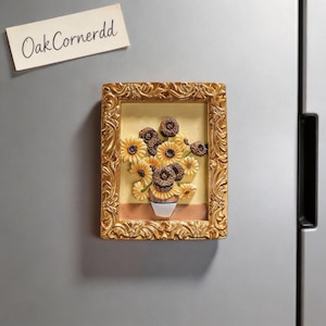 May include: A framed magnet featuring a still life of sunflowers in a vase, reminiscent of Van Gogh's style. The frame is gold, and the sunflowers are yellow and brown. The text "OakCornerdd" is on a separate tag.