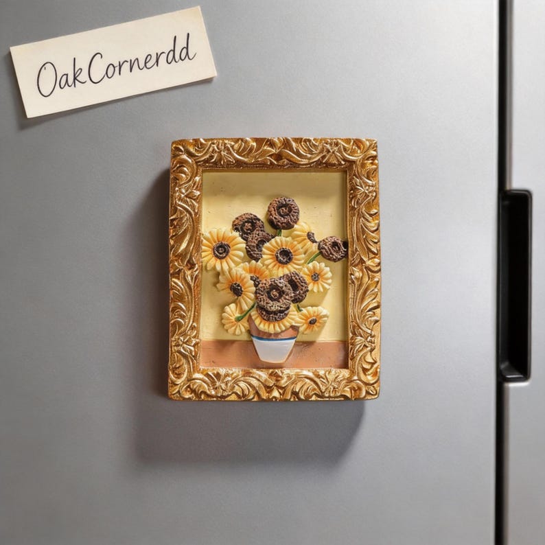 May include: A framed magnet featuring a still life of sunflowers in a vase, reminiscent of Van Gogh's style. The frame is gold, and the sunflowers are yellow and brown. The text "OakCornerdd" is on a separate tag.