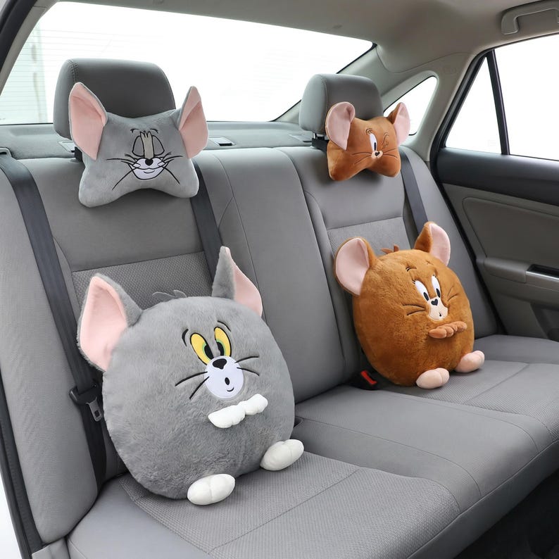 May include: Car seat accessories featuring cartoon characters. The image shows four plush pillows and headrest covers with the likeness of Tom and Jerry. The pillows are gray and brown, with pink ears and white accents. The headrest covers are gray and brown.