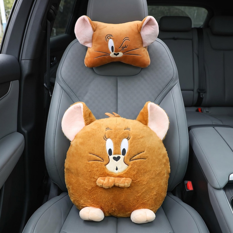 May include: Two plush car seat cushions shaped like a cartoon mouse. The headrest cushion is rectangular, and the seat cushion is round. Both are brown with pink ears and mouse features.