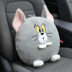 May include: A plush, gray cat-shaped pillow with pink inner ears, yellow eyes, and a white bow tie. The pillow is round and sits on a car seat, offering a whimsical design for car decor.