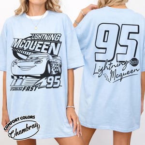 May include: Pale blue t-shirt with a graphic of Lightning McQueen from the film Cars. The front design shows the character, the text "Lightning McQueen," and "95." The back has a large "95" and "Lightning McQueen" with a lightning bolt.