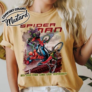 May include: Mustard-colored t-shirt featuring a Spider-Man graphic. The design includes Spider-Man in action with villains, the text "SPIDER-MAN," and the phrase "WITH GREAT POWER COMES GREAT RESPONSIBILITY."
