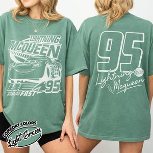 May include: Light green t-shirt with Lightning McQueen design. The front features the character and text, the back has a large "95" and "Lightning McQueen" text. The shirt is a Comfort Colors brand.