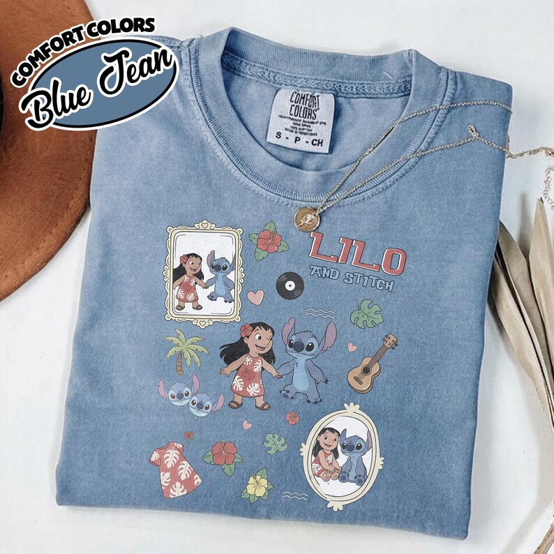 Puede incluir: Camiseta Comfort Colors azul vaquero con las palabras "Lilo and Stitch" y gr&aacute;ficos de dibujos animados de Lilo y Stitch. La camiseta tiene cuello redondo y mangas cortas. Un collar dorado est&aacute; drapeado sobre la camiseta.