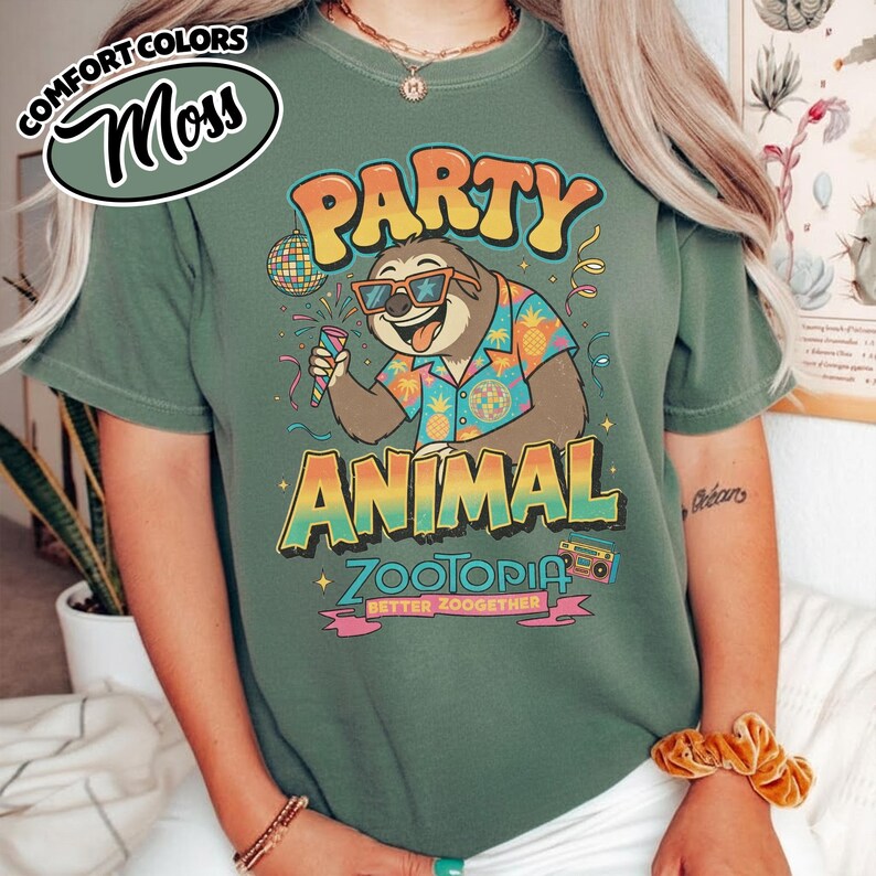 May include: Moss green t-shirt with a colorful graphic of a sloth wearing sunglasses and a Hawaiian shirt, holding a microphone. The text reads "PARTY ANIMAL ZOOTOPIA BETTER ZOOGETHER".