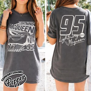 May include: Charcoal grey t-shirt with a Lightning McQueen design. The front shows the character, number 95, and "Think Fast." The back has a large white "95" and "Lightning McQueen" text. The shirt is a Comfort Colors Pepper style.