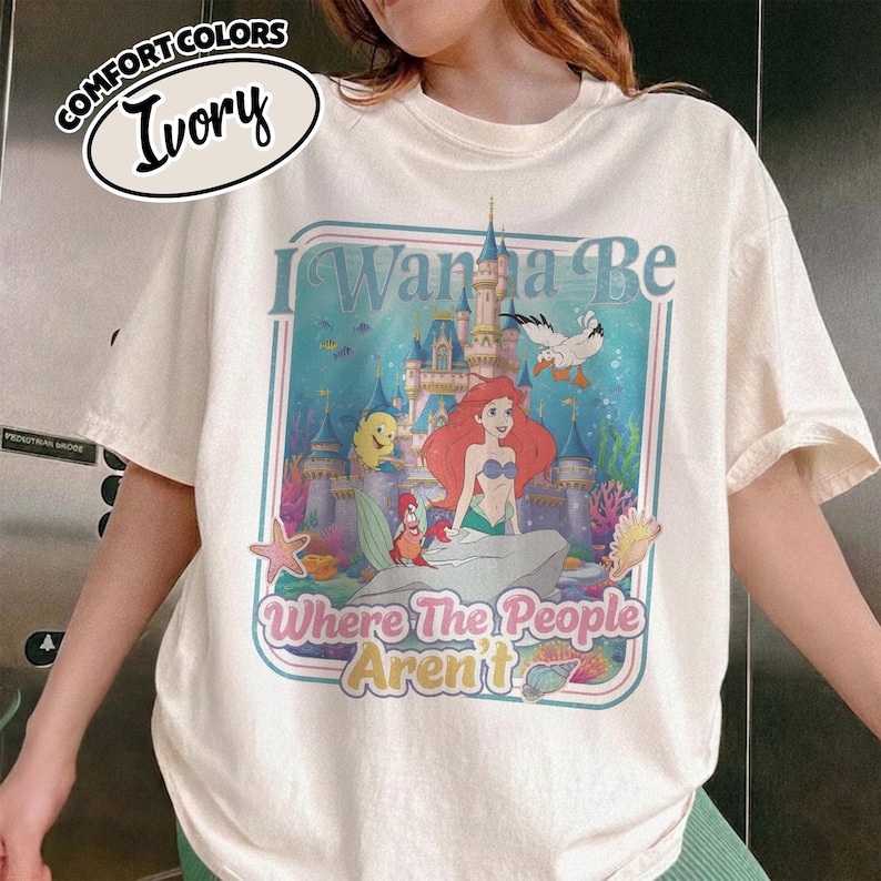 Puede incluir: Camiseta color marfil con un gr&aacute;fico de Ariel de La Sirenita. El gr&aacute;fico incluye un castillo, peces y el texto "I Wanna Be Where The People Aren't". La camiseta es de la marca Comfort Colors.