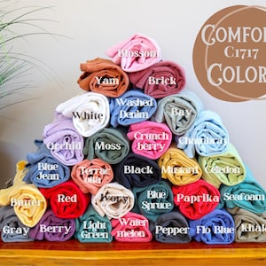 May include: A display of rolled-up t-shirts in various colors, including white, blue, red, and green. The image includes a color chart with names like "Blossom" and "Khaki" and the text "COMFORT COLORS C1717".