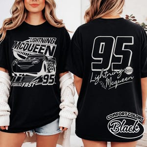 May include: Black t-shirt with Lightning McQueen design. The front shows the character, number 95, and "Lightning McQueen". The back has a large "95" and the character's name. The shirt is labelled "Comfort Colors Black". A classic tee for fans of the Cars movie.