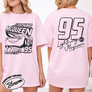 May include: Pale pink t-shirt with Lightning McQueen graphics. The front shows the character and text "Lightning McQueen", "95", and "Think Fast". The back has a large "95" and "Lightning McQueen" text. The shirt is from Comfort Colors.