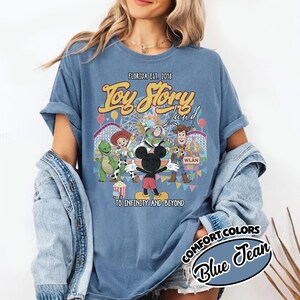 May include: Blue jean-coloured t-shirt with a graphic of Toy Story characters and the text "Toy Story Land" and "To Infinity and Beyond." The shirt also includes the text "Florida Est. 2018" and "Comfort Colors Blue Jean."