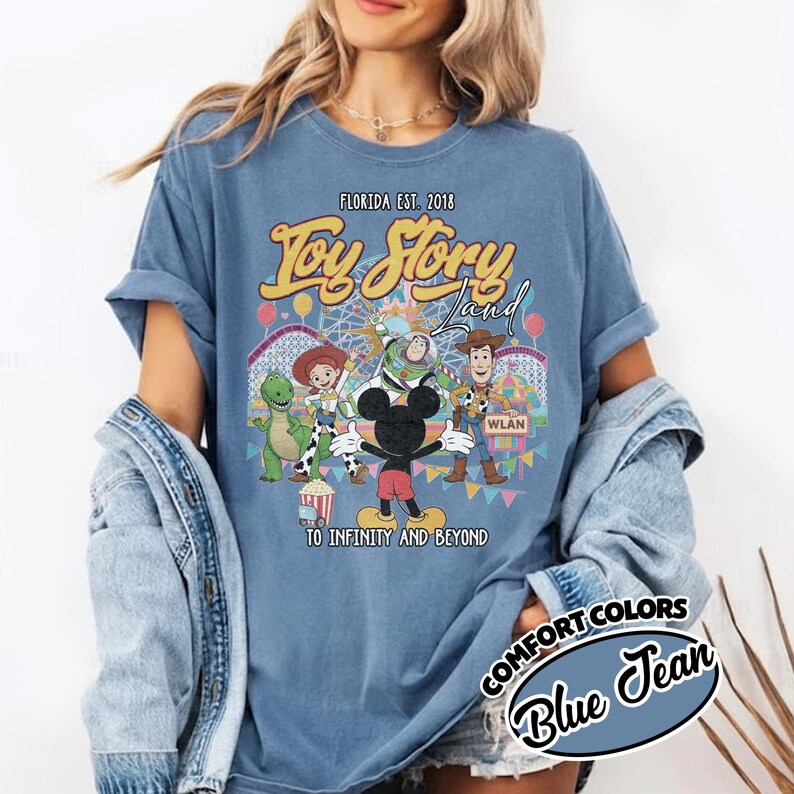 May include: Blue jean-coloured t-shirt with a graphic of Toy Story characters and the text "Toy Story Land" and "To Infinity and Beyond." The shirt also includes the text "Florida Est. 2018" and "Comfort Colors Blue Jean."