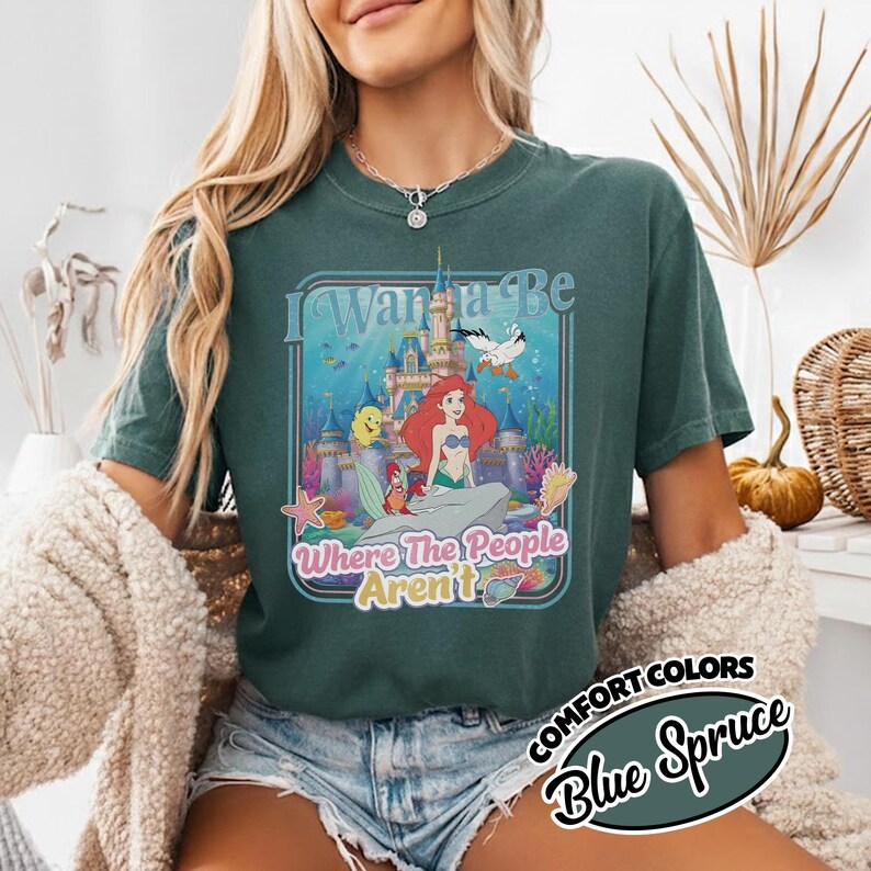 Puede incluir: Camiseta Comfort Colors azul abeto con un gr&aacute;fico colorido de Ariel de La Sirenita. El gr&aacute;fico incluye el texto "I Wanna Be Where The People Aren't". La camiseta tiene mangas cortas y cuello redondo.