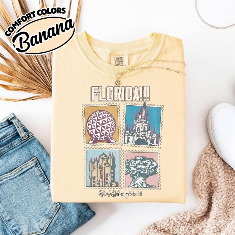 Może przedstawiać: Ż&oacute;łta koszulka z nadrukiem przedstawiającym zabytki Florydy. Koszulka zawiera napis "FLORIDA!!!" nad czterema obrazami w stylu znaczka pocztowego Spaceship Earth, Cinderella Castle, Tower of Terror i Tree of Life. Pod obrazami wydrukowano słowa "Walt Disney World".